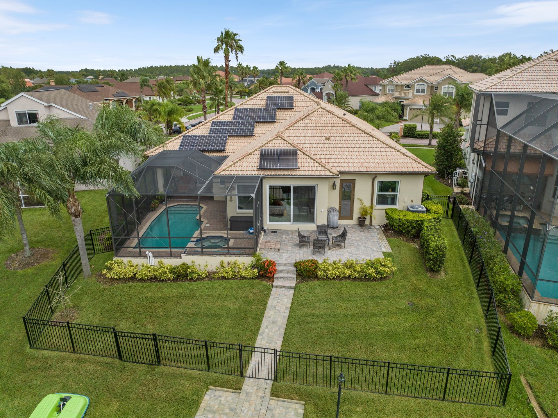 Aerial view of a suburban house with solar panels, pool, and fenced backyard with patio.