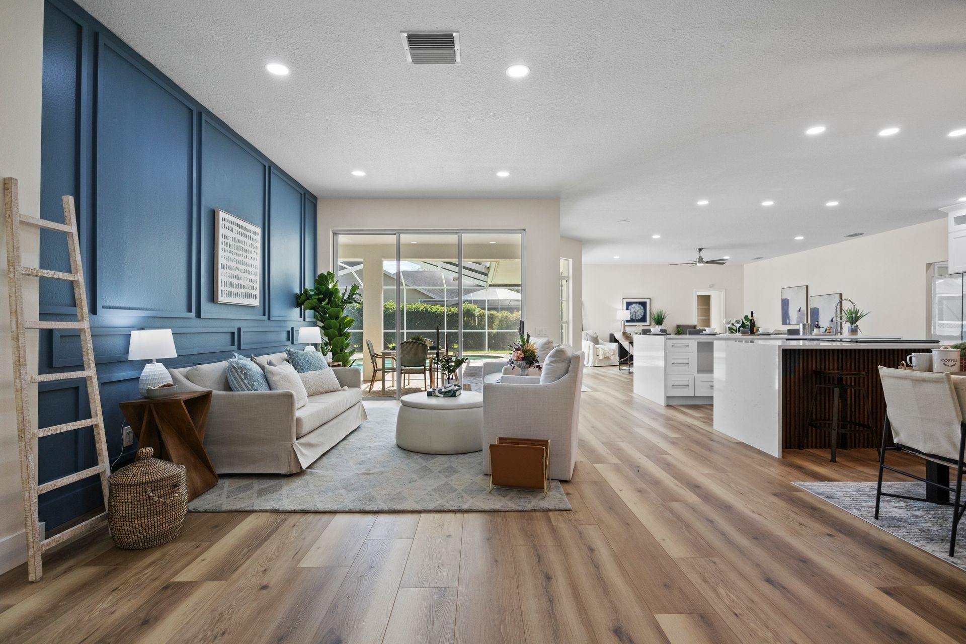 Modern living room with wood flooring, blue accent wall, and cozy seating area near large windows.